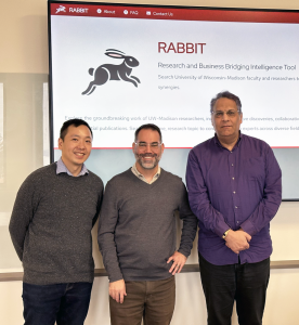 Jason Lo, Kyle Cranmer, and Abe Megahed standing in front of a screen with the RABBIT home page projected on it.