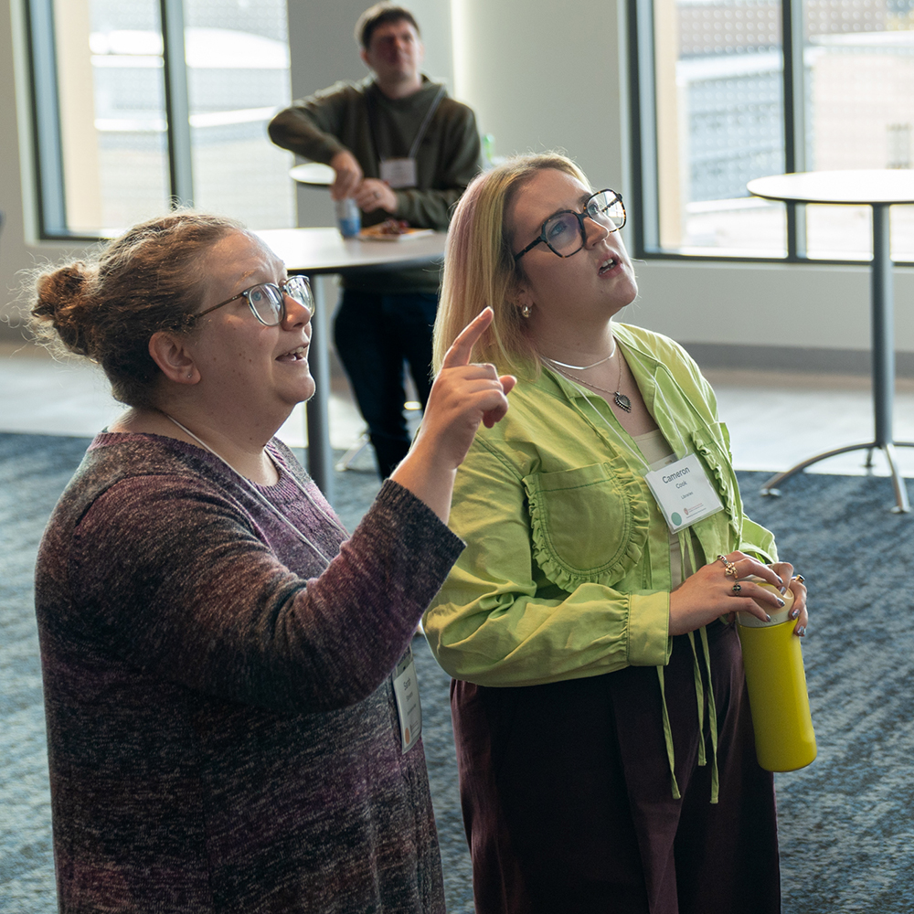 The image shows three people looking at something in the distance. One woman is pointing at it, while the other two people are looking.