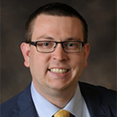 Photo of Matt Sinclair. He has dark hair and glasses, and he is wearing a suit and tie.