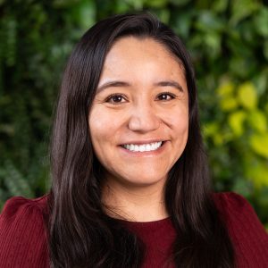 Head shot of Alejandra Quintos. She has long brown hair, and she is wearing a red shirt.