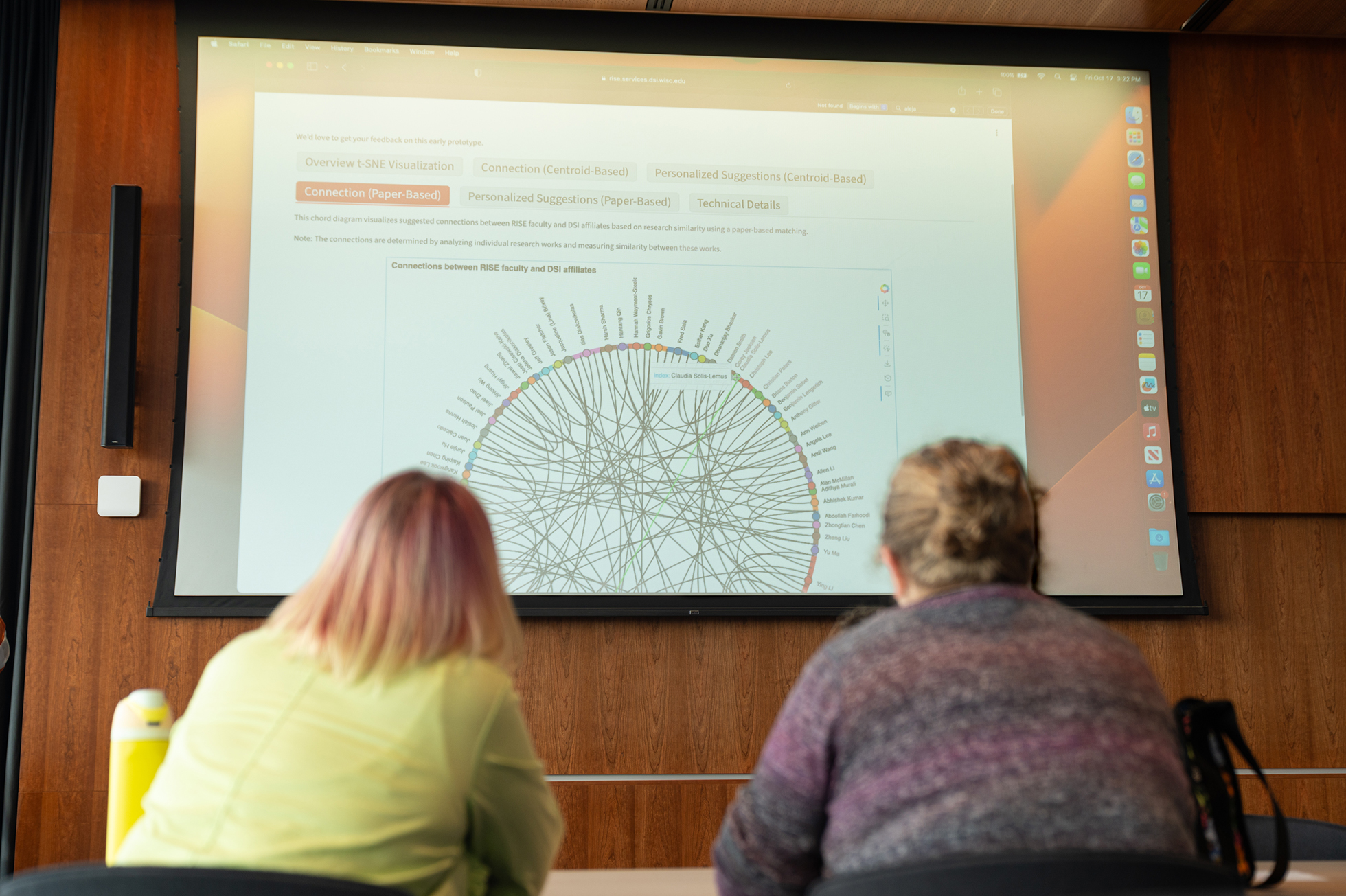 Rear view of two people looking at a data visualization projected on a large screen